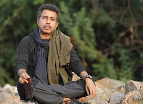 Pankaj Jha sitting on rocks outdoors, wearing a scarf