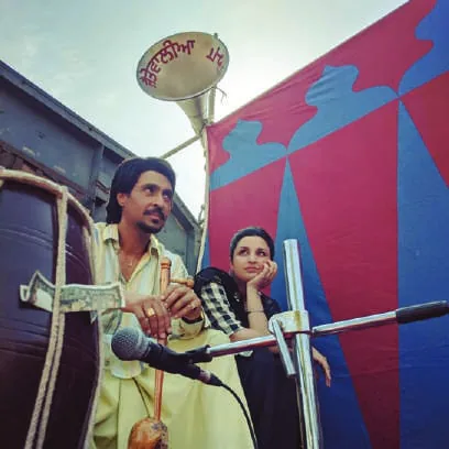 Diljit Dosanjh and Parineeti Chopra seated on a vehicle with a microphone and loudspeaker, in a scene from the film