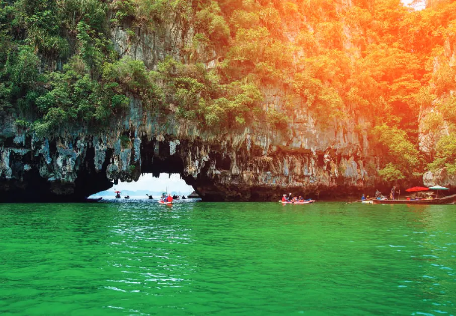 Kayaks paddling towards a sea cave in green water below cliffs