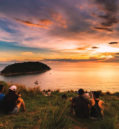 People watching the sunset over the sea from a hillside