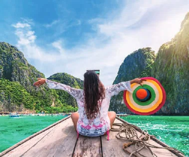 A woman with arms outstretched at the bow of a boat among limestone islands