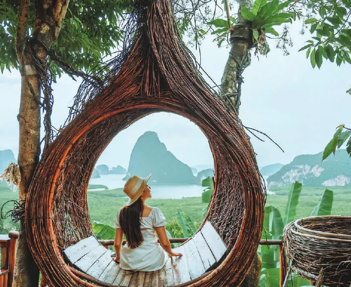 A woman sitting in a giant woven nest overlooking limestone islands