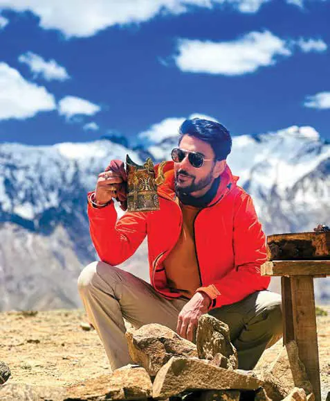 Ranveer Brar in a red jacket, seated outdoors against snow-capped mountains