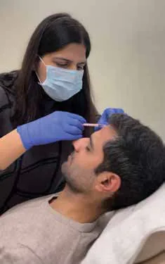 A doctor in gloves and a mask injecting a man’s forehead