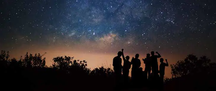 Silhouetted people under a starry night sky