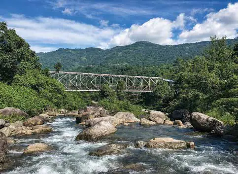 A steel bridge over a rocky river surrounded by forest
