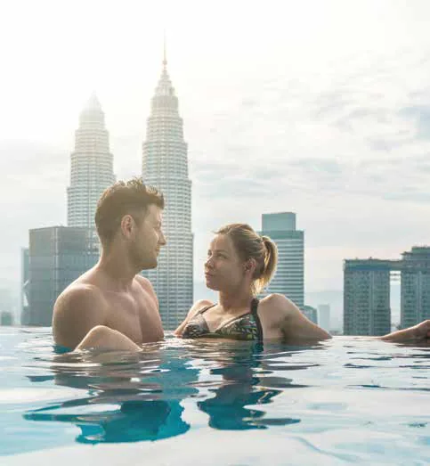 A couple in a rooftop infinity pool with skyscrapers behind
