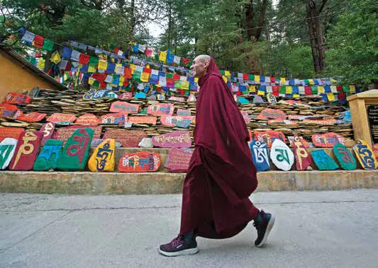 A Buddhist monk in maroon robes walking past painted prayer stones and prayer flags
