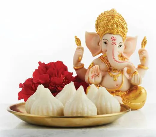 Steamed modaks on a brass plate before a Ganesha idol, with red flowers