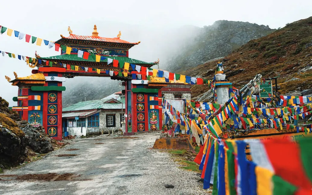 A colourful ornate gateway over a road lined with prayer flags, with misty hills behind
