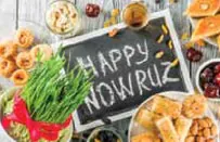 Festive sweets and sprouts around a chalkboard reading Happy Nowruz