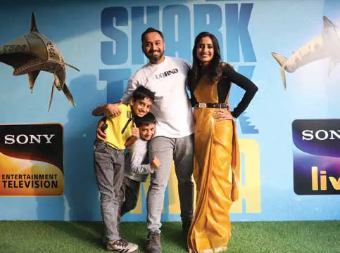 Vineeta Singh with a man and two young boys in front of a Shark Tank India backdrop