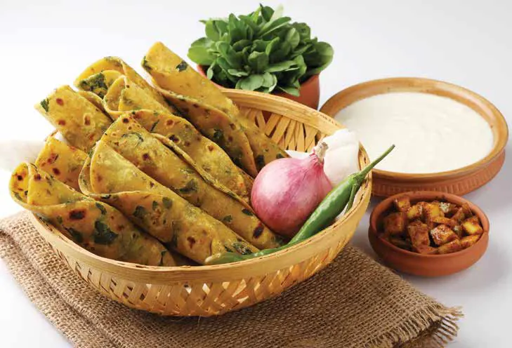 Rolled palak theplas in a basket with curd, onion and chilli