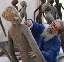 A bearded sculptor working on a tall clay figure