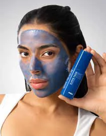 A woman wearing a blue face mask holding a skincare bottle