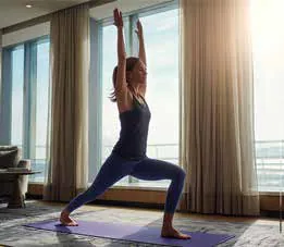 A woman in a yoga pose on a mat beside tall windows