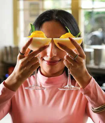 A woman holding two glasses of mango sorbet in front of her eyes