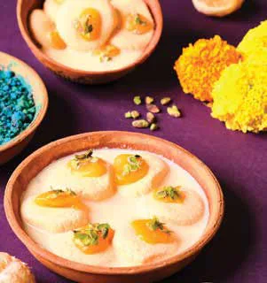 Bowls of rasmalai beside heaps of coloured powder
