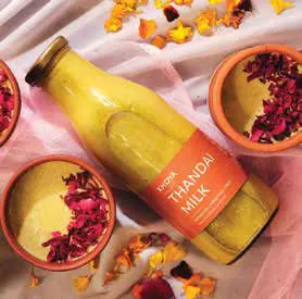 A bottle of thandai milk beside bowls of rose petals and spices