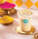 A cup of thandai beside bowls of coloured powder