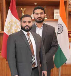 Two men in suits standing before flags