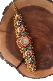 An ornate watch with an emerald dial on a wooden block